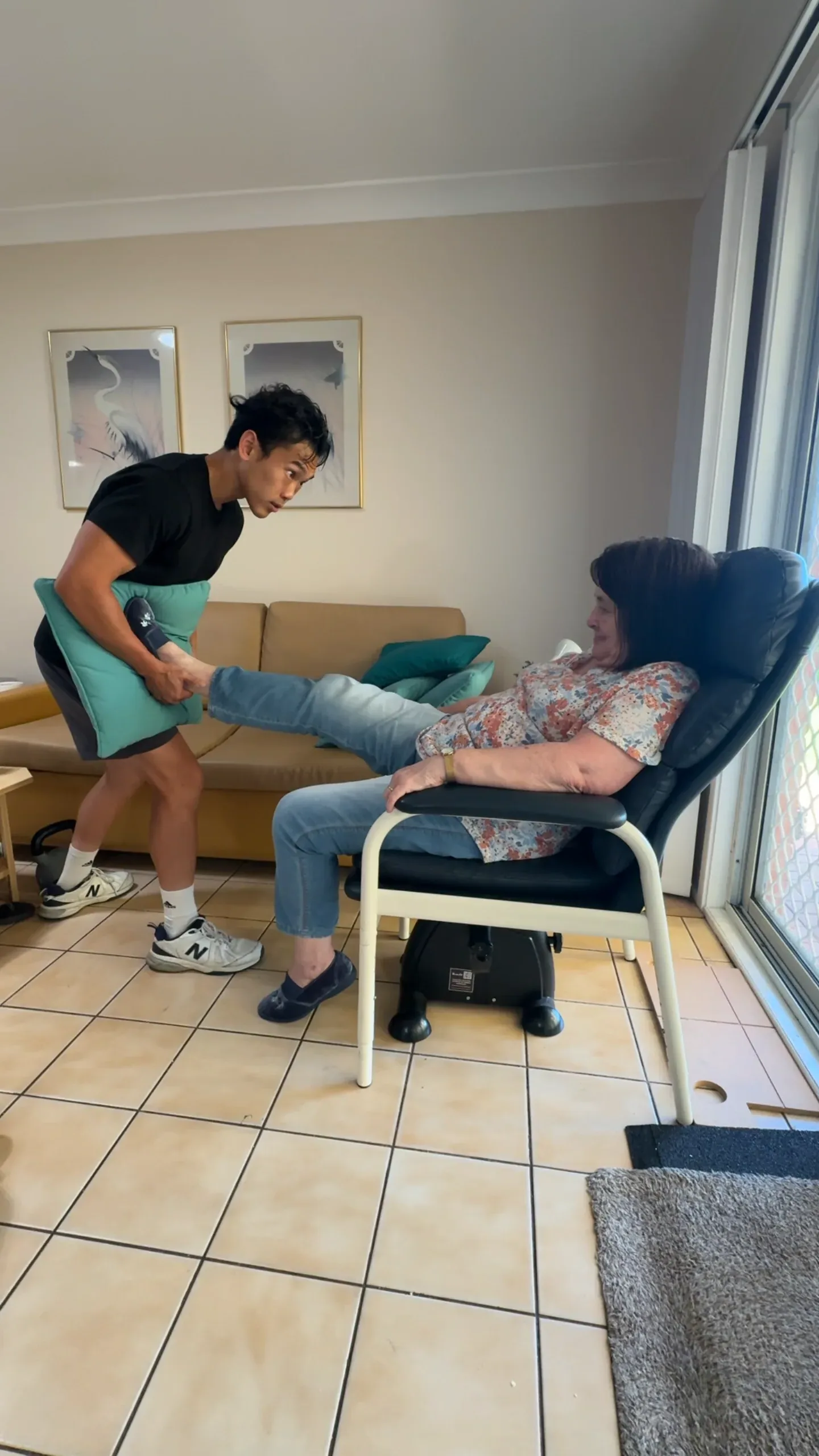 A Drift Health physiotherapist guiding a seated leg press for a woman in her armchair at home