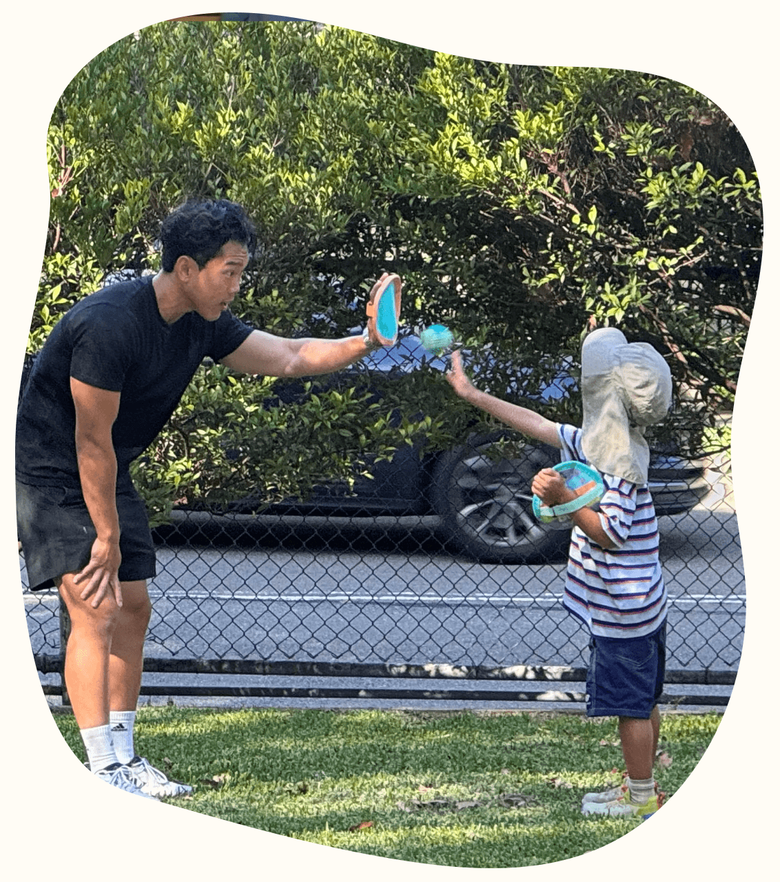 A therapist and a young child playing a catching game on the grass