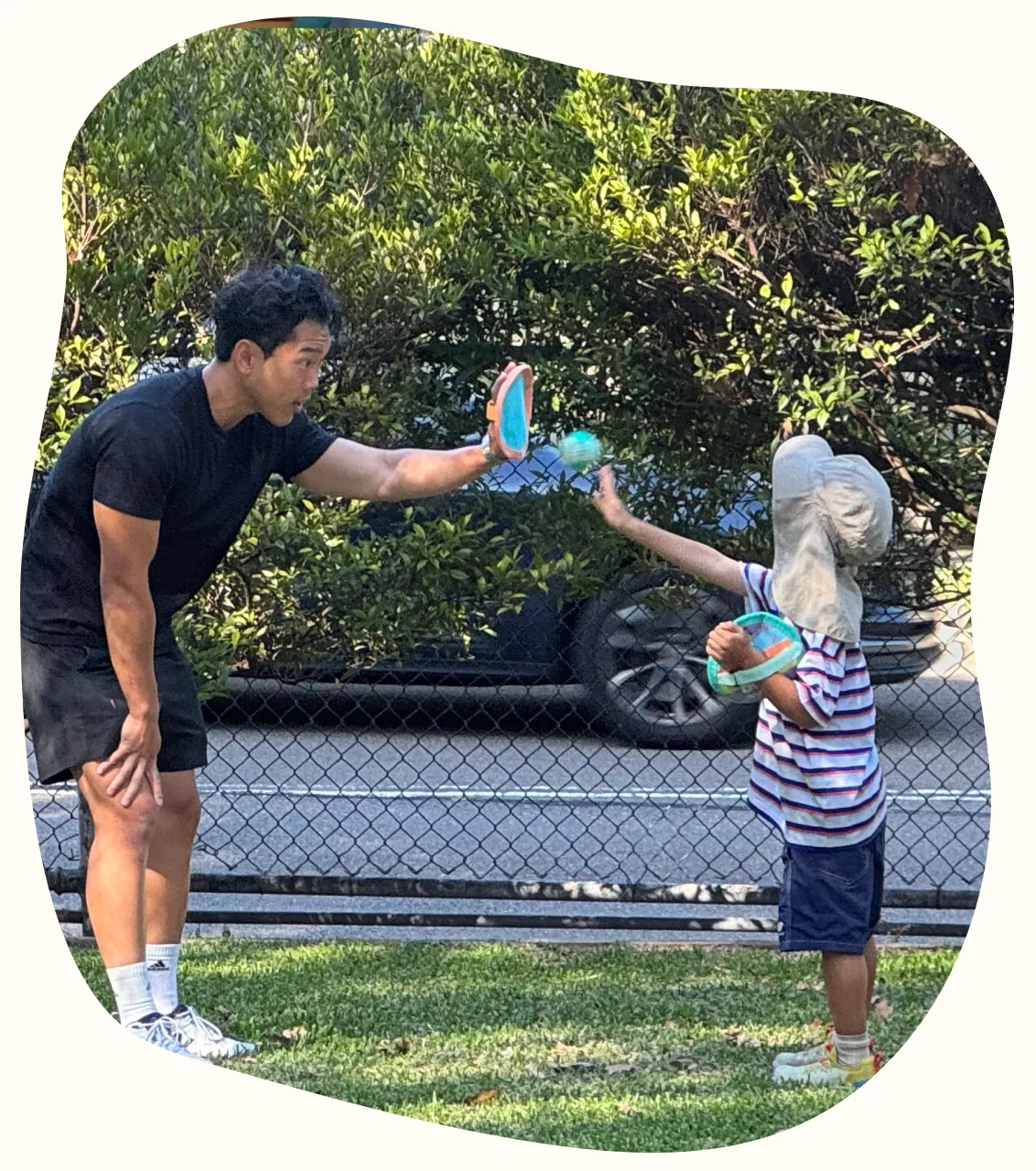 A therapist and a young child playing a catching game on the grass
