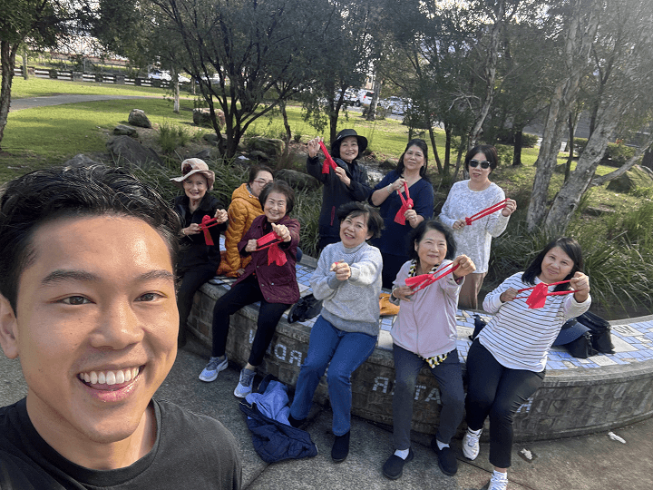 Clinician taking a smiling selfie with a group of adults holding resistance bands in a park