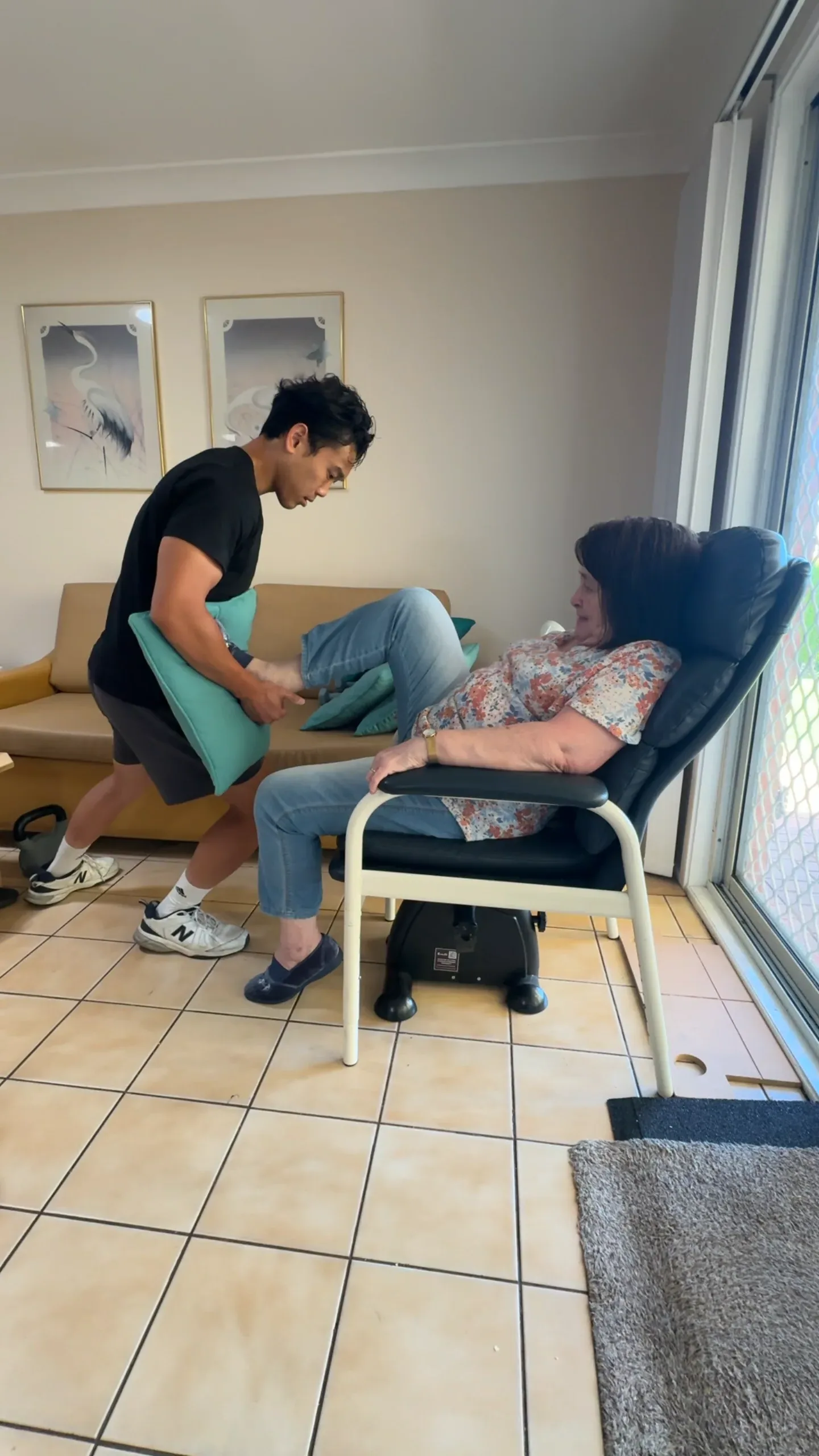 A Drift Health physiotherapist supporting a seated leg movement for a woman in her armchair
