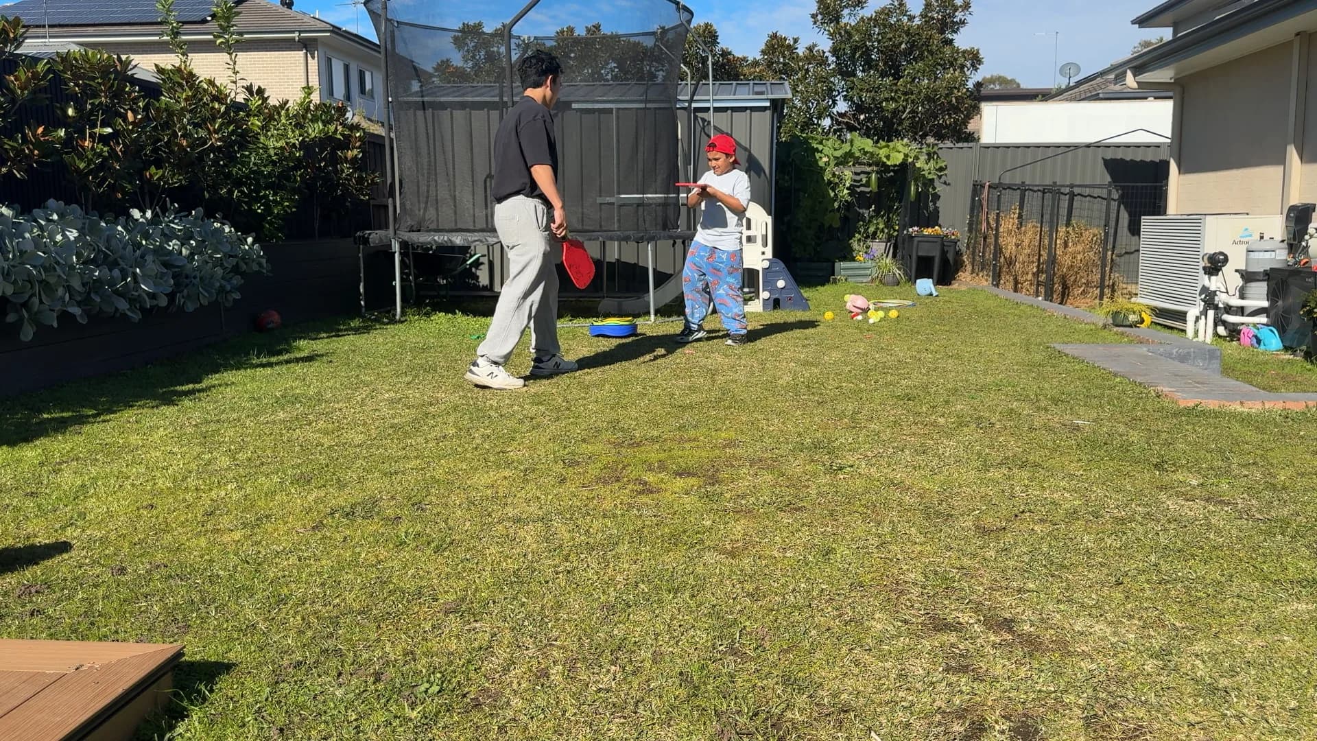 A child practising a racquet swing with a therapist in the backyard