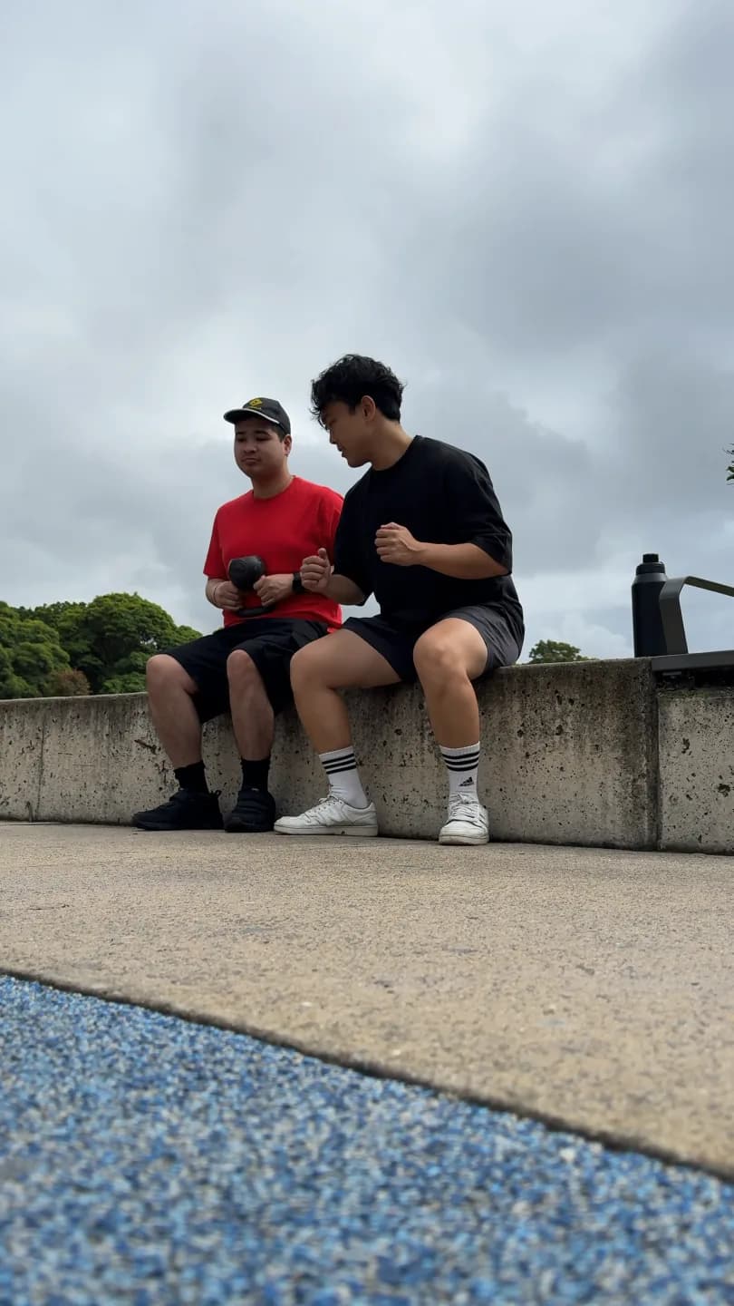 Clinician and adult sitting on a low outdoor wall, the adult holding a dumbbell