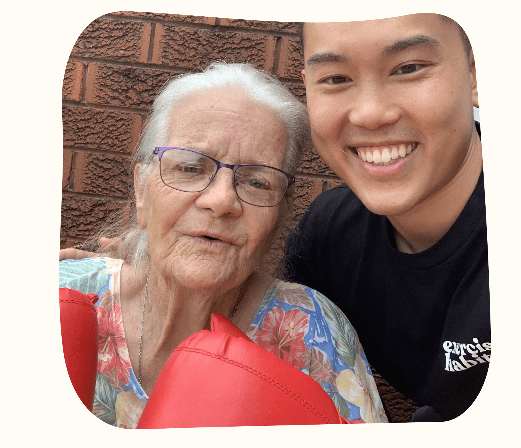 An older woman in boxing gloves smiling beside a Drift Health exercise physiologist at home
